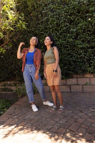 Diverse friends laughing and looking up on sunlit backyard patio, casual summer