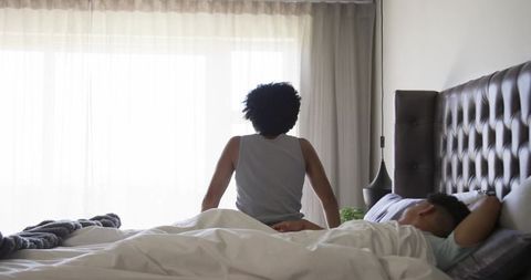Morning reflection man sitting on bed gazing through sheer curtains in minimalist bedroom