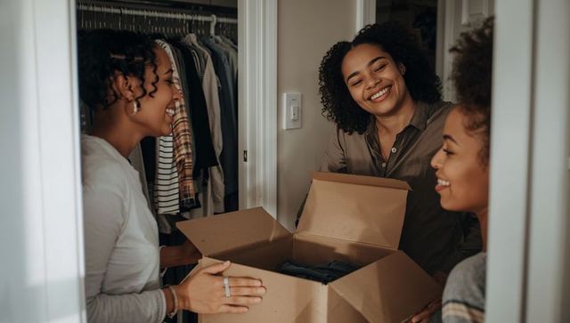 African american women smiling while packing wardrobe box in home closet during move