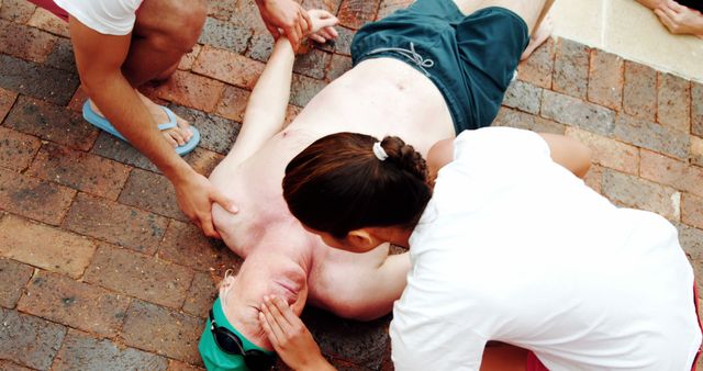 A person is performing CPR on a Caucasian middle-aged man lying on the ground, with another individual looking on, indicating a medical emergency situation. Quick response with cardiopulmonary resuscitation can be crucial in saving lives during such critical incidents.