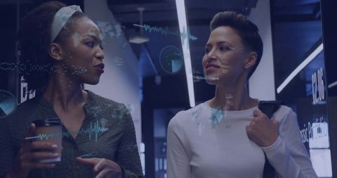 Two professionals walking and discussing with holographic data overlays in modern office
