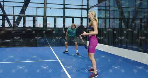 Rooftop padel doubles on blue glass court with female in pink, male in teal, daylight