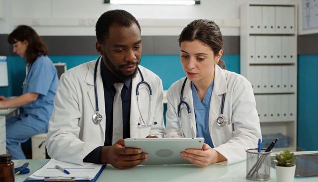 Doctors reviewing patient records on tablet in clinic collaborating on care plan