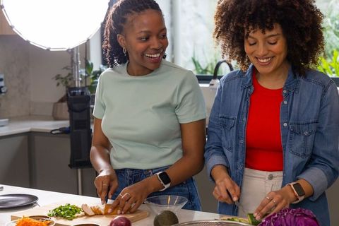 African American women preparing colorful salad together in bright home kitchen with studio lights