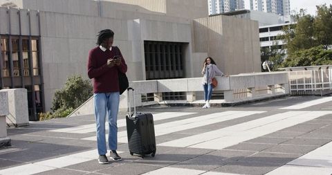 Urban commuters using smartphones while waiting with suitcase on rooftop plaza