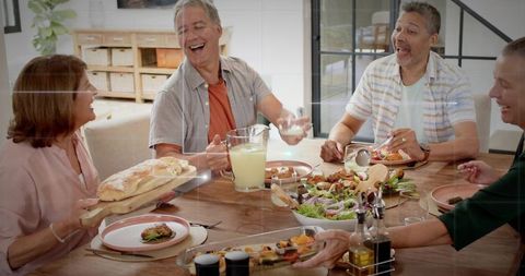 Friends laughing and sharing homemade meal around wooden table with salad and bread