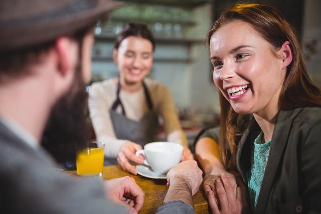 Waitress serving a cup of coffee to smiling customers in a cozy cafe. Ideal for use in hospitality, service industry, coffee shop promotions, and social interaction themes.