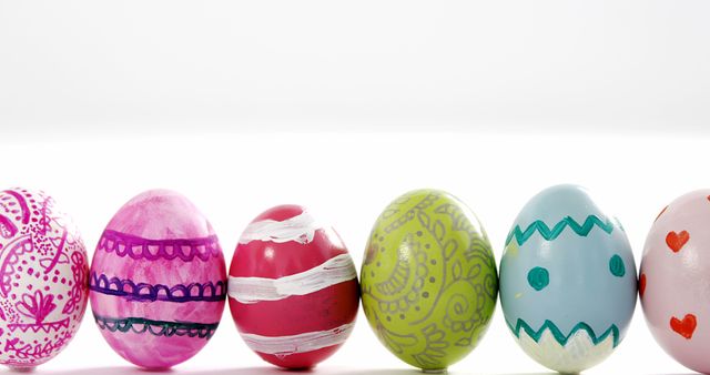 A variety of colorful, decorated Easter eggs are lined up against a white background, with copy space. Each egg features unique patterns and designs, symbolizing the festive spirit of the Easter holiday.