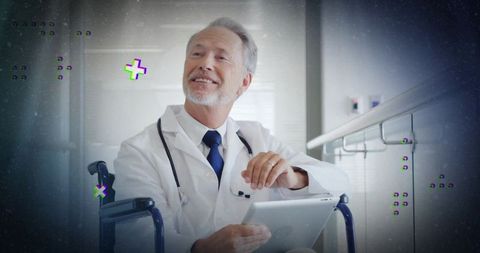 Smiling senior physician with stethoscope holding tablet sitting wheelchair in hospital corridor
