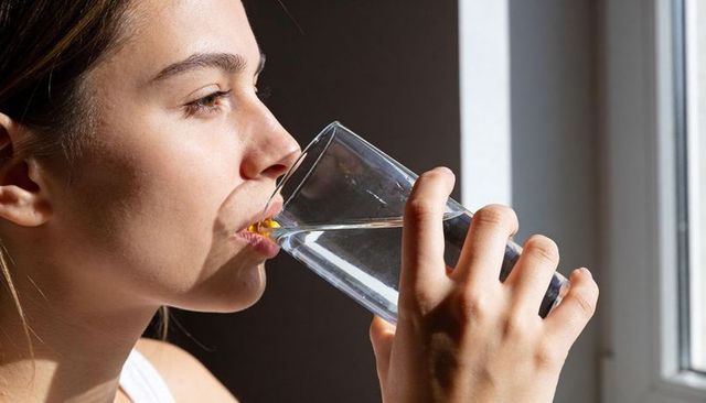 Young woman drinking water in sunlight closeup profile with white tank strap