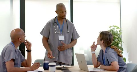 Medical team collaborating in clinic meeting with laptop and stethoscope discussing care