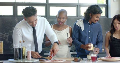 Diverse friends preparing homemade pizza together in modern kitchen celebration