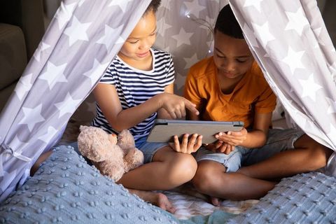 Siblings enjoying tablet time in cozy star teepee