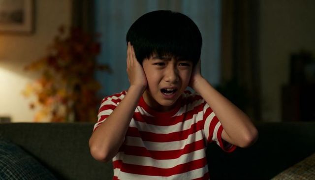 Young boy covering ears on sofa at night expressing distress and sensory overload
