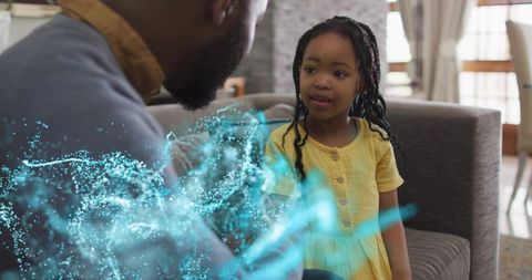 Father leaning toward daughter watching blue hologram on sofa, family bonding