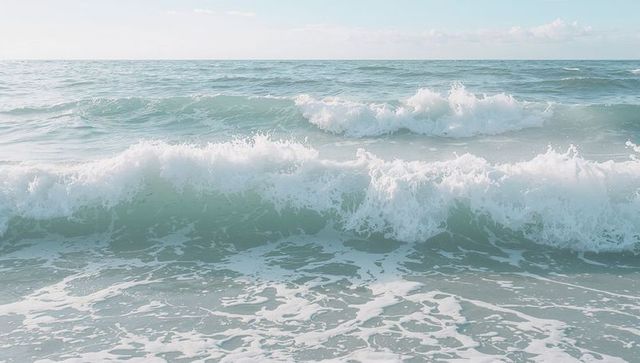 Calm turquoise ocean waves breaking onto shore with white foam and distant horizon