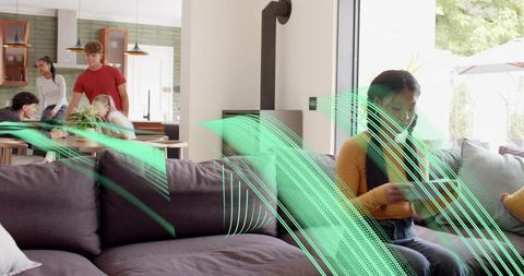 Young woman browsing phone on sofa while friends socializing in modern open-plan home