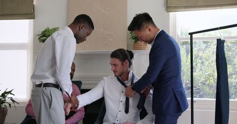 Groom preparing with friends adjusting tie for special day