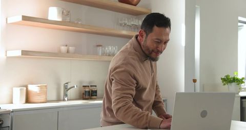 Asian Man Working on Laptop in Minimalist Kitchen with Natural Light