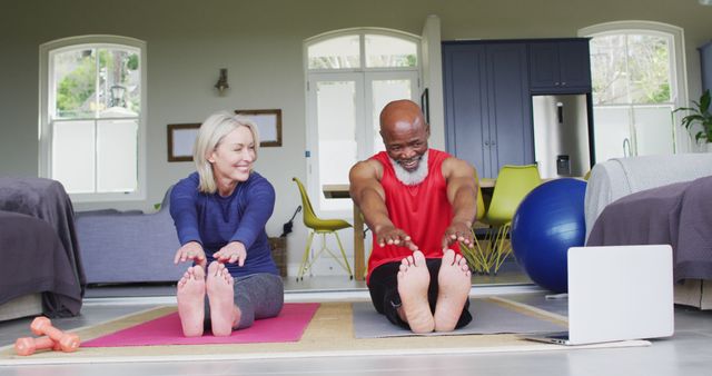 Senior couple exercising together on yoga mats at home. They are smiling while stretching towards their feet, indicating a positive mood and healthy lifestyle. Can be used for advertising fitness programs designed for seniors, articles about home workouts, or promoting healthy aging and wellness routines.