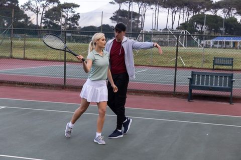 Tennis coach guiding female player through forehand technique on outdoor court during lesson