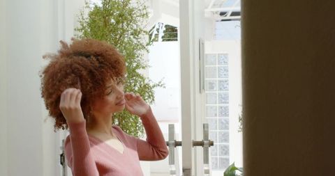 African american woman adjusting curly hair by glass door in sunlit modern foyer