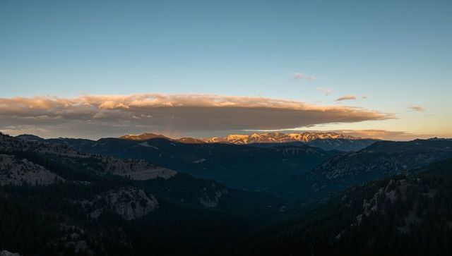 Golden hour snowcapped peaks glowing over deep alpine valley beneath flat lenticular cloud