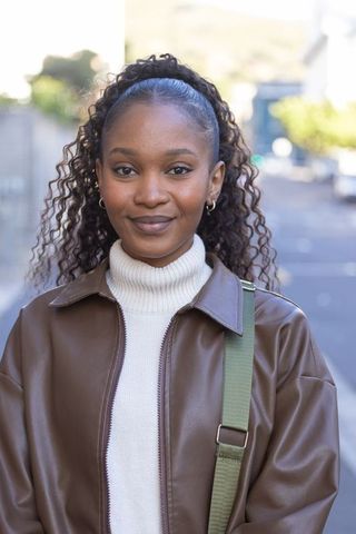 Smiling african american woman wearing brown leather jacket and green crossbody strap
