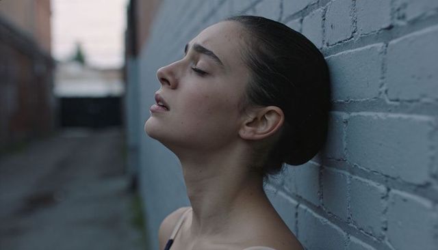 Young woman leaning against painted brick wall, eyes closed, urban moody closeup portrait