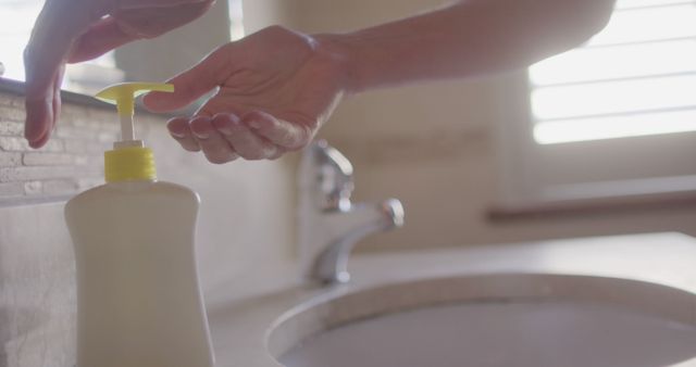 Image shows a closeup of hands using a pump bottle to dispense liquid soap in a bathroom. Perfect for promoting hygiene, cleaning products, instructional guides on proper handwashing techniques, and health awareness campaigns.