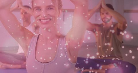 Smiling woman practicing yoga in group class with purple mats and dreamy pink bokeh overlay