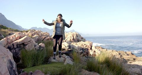 Woman Engaging in Joyful Adventure on Rocky Terrain by Ocean Shore