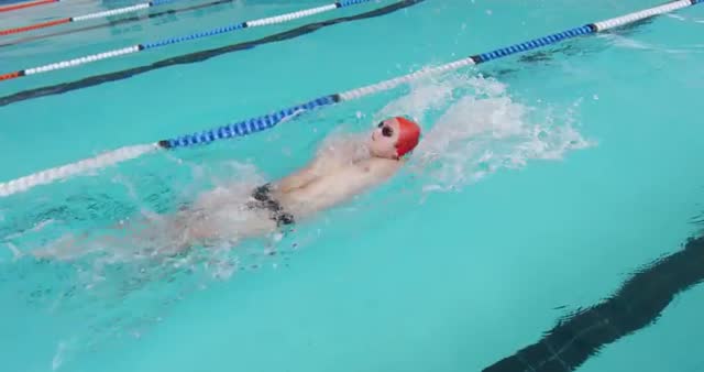 Caucasian male swimmer is seen racing in a pool, demonstrating the backstroke technique, with clear blue water and distinctive eye-catching strokes. Useful for illustrating competitive swimming, sports training materials, or fitness-related content emphasizing aquatic skills and water-based recreation.