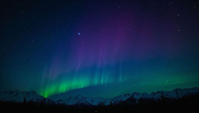 Vibrant northern lights dancing over snow-capped mountains and starry arctic sky