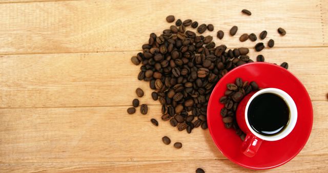 A red coffee cup filled with black coffee sits beside a pile of coffee beans on a wooden surface, with copy space. The arrangement invites a sense of warmth and energy, ideal for themes related to morning routines or coffee culture.
