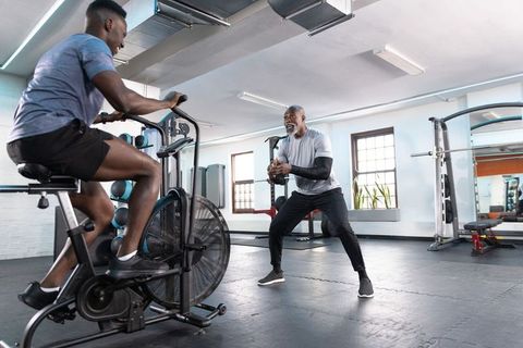 African american trainer coaching athlete on air bike during functional strength circuit