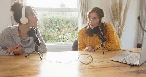 Recording cozy home podcast with diverse female cohosts wearing headphones and mics