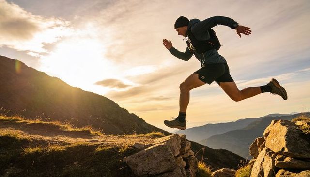 Trail runner leaping across rugged mountain ridge at golden hour sunrise with backpack