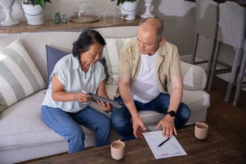 Asian senior couple reviewing bills and managing finances at home with tablet