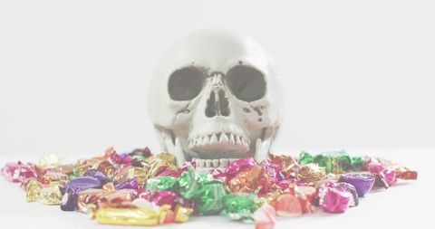 Ceramic skull sitting among colorful foil-wrapped candies on bright white tabletop