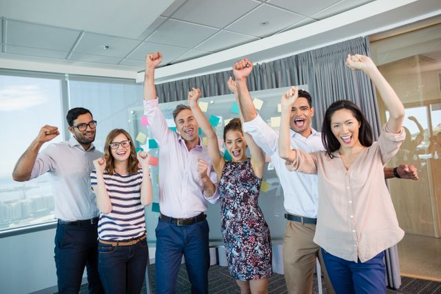Group of business colleagues celebrating success with raised fists in modern office. They look joyful and united, symbolizing teamwork and achievement. Useful for depicting corporate culture, employee motivation, and team success in marketing materials, business presentations, and company websites.