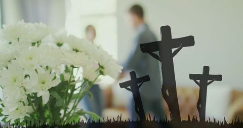 White memorial bouquet on window glass with blurred couple and crucifix silhouettes soft bokeh
