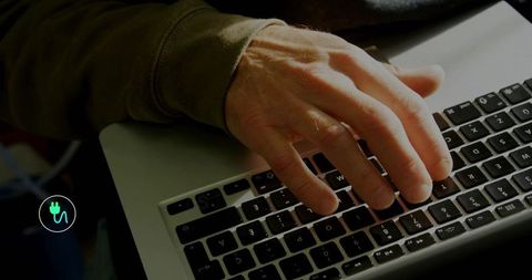 Mature woman typing on laptop keyboard in moody home workspace with olive sleeve