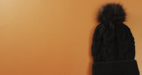 Black Knitted Hat with Faux Fur Pom Pom on Orange Background