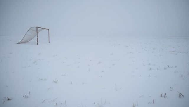 Rusted soccer goal standing in snow-covered field, sagging net under foggy winter sky