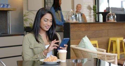 Woman using smartphone at cozy cafe table with coffee and croissant