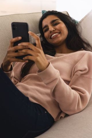 Smiling Woman Relaxing on Couch Browsing Smartphone at Home