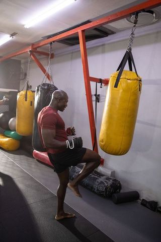 African american athlete practicing knee strikes on heavy bag in boxing gym, focused training
