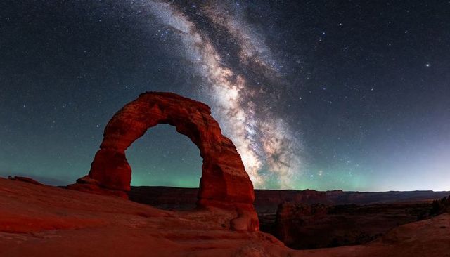 Milky way over freestanding redrock arch on desert ledge at night, starfield panorama
