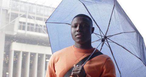 African-american man holding transparent umbrella in rainy city wearing orange sweater